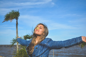 Young woman blissfully smiling by the ocean with colorful sunscreen on nose. 